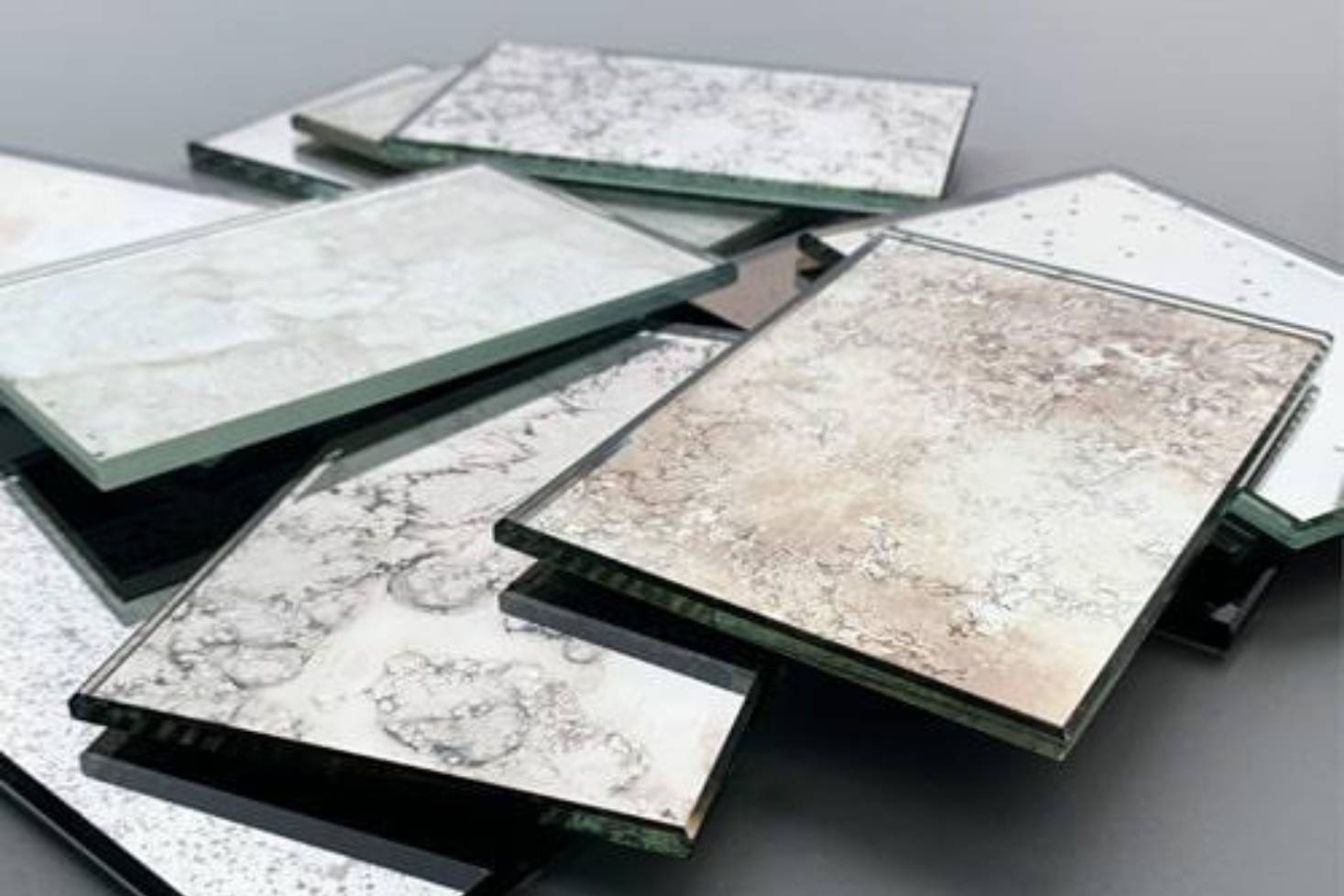 Stack of decorative antique mirror glass samples with various textures and finishes.