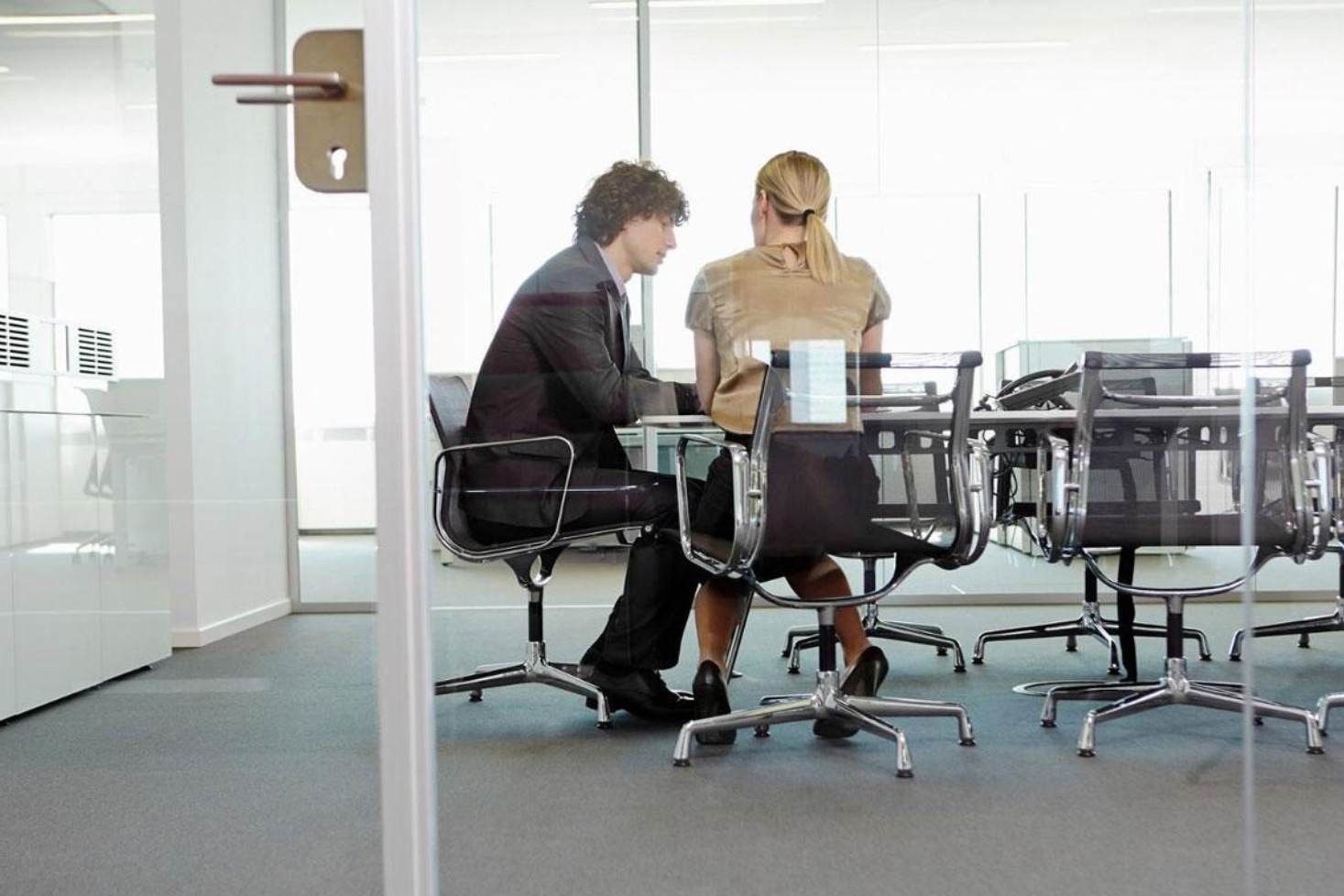 Two employees hold a meeting in a glass-partitioned office