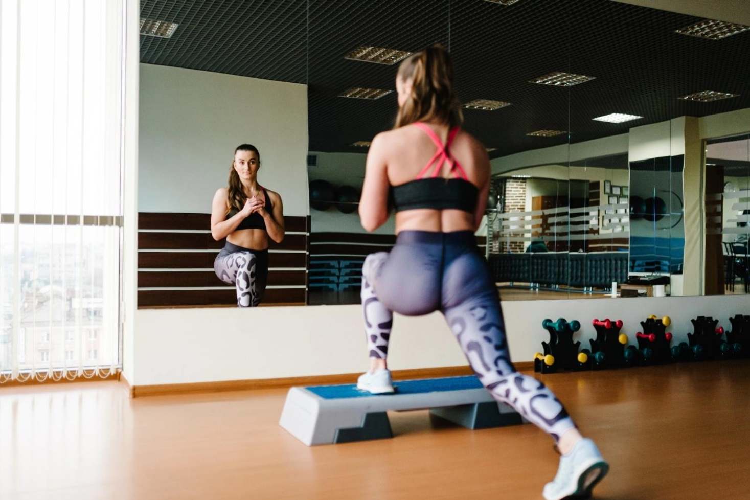 Young woman is doing exercise in the gym, in front of a mirror.
